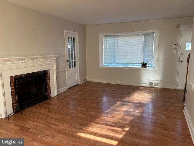 unfurnished living room with hardwood / wood-style flooring and a brick fireplace