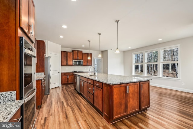 kitchen featuring an island with sink, appliances with stainless steel finishes, light stone counters, and decorative light fixtures