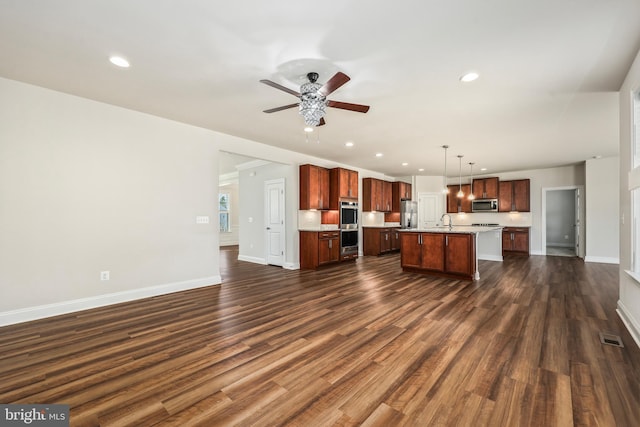 kitchen with sink, dark wood-type flooring, stainless steel appliances, an island with sink, and decorative light fixtures