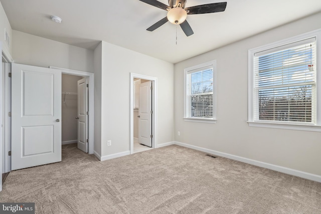 unfurnished bedroom featuring ceiling fan, a closet, a spacious closet, and light carpet