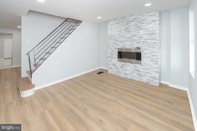 unfurnished living room featuring a stone fireplace and light hardwood / wood-style floors