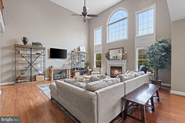 living room featuring a high ceiling, a glass covered fireplace, hardwood / wood-style flooring, and baseboards