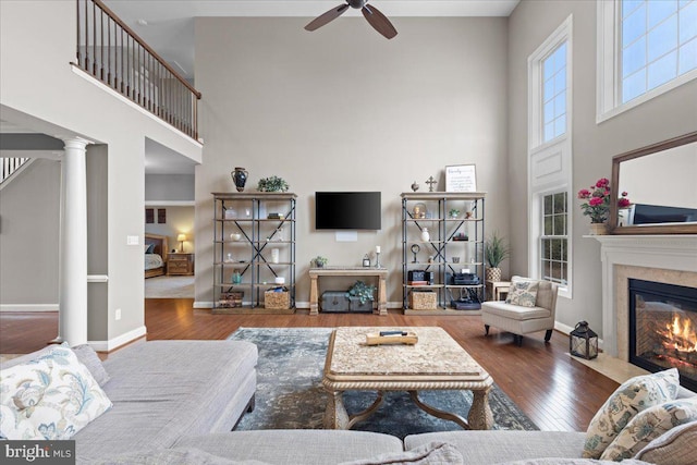 living area featuring hardwood / wood-style floors, a premium fireplace, a high ceiling, and ornate columns