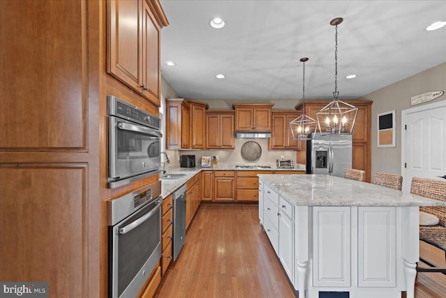 kitchen with pendant lighting, stainless steel appliances, light wood-style floors, a sink, and a kitchen island