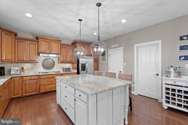 kitchen with appliances with stainless steel finishes, brown cabinetry, a kitchen island, and dark wood-type flooring