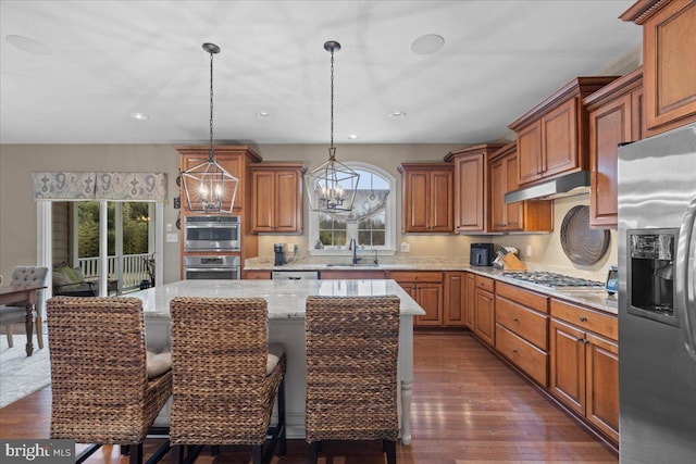 kitchen with a chandelier, under cabinet range hood, stainless steel appliances, a sink, and dark wood-style floors