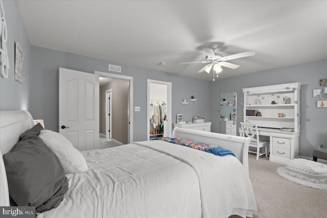 carpeted bedroom with a spacious closet, visible vents, and a ceiling fan