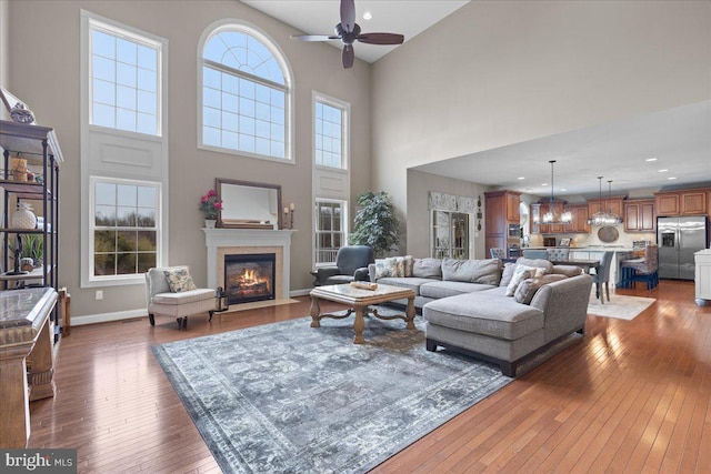 living area featuring hardwood / wood-style flooring, recessed lighting, a fireplace with flush hearth, a ceiling fan, and baseboards