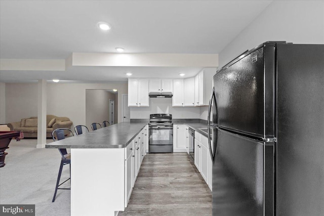 kitchen featuring dark countertops, a breakfast bar area, under cabinet range hood, black appliances, and white cabinetry