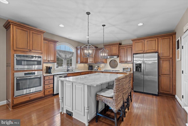 kitchen featuring brown cabinetry, appliances with stainless steel finishes, dark wood-type flooring, a center island, and a sink