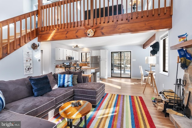 living room with beam ceiling, a high ceiling, and light wood-type flooring