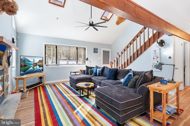 living room with ceiling fan, a stone fireplace, vaulted ceiling with skylight, and light wood-type flooring