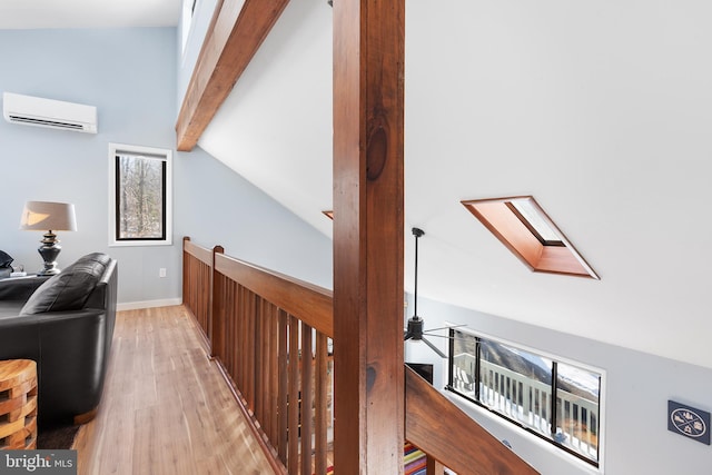 hall featuring a wall mounted air conditioner, vaulted ceiling with skylight, and light hardwood / wood-style floors