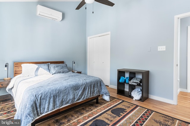 bedroom with hardwood / wood-style floors, a wall mounted AC, ceiling fan, and a closet