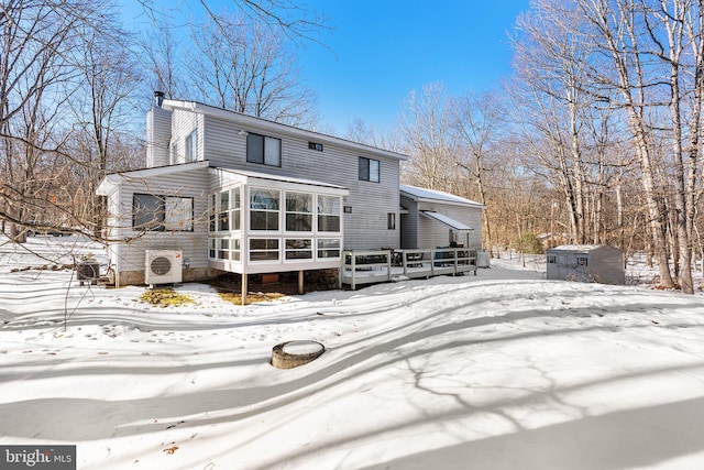 snow covered back of property with a storage shed, a sunroom, a deck, and ac unit