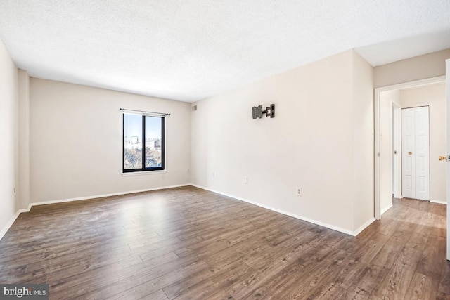 empty room featuring a textured ceiling, dark wood-style flooring, and baseboards