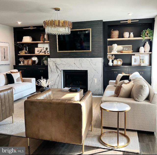 living room featuring hardwood / wood-style flooring, a premium fireplace, built in shelves, and a notable chandelier