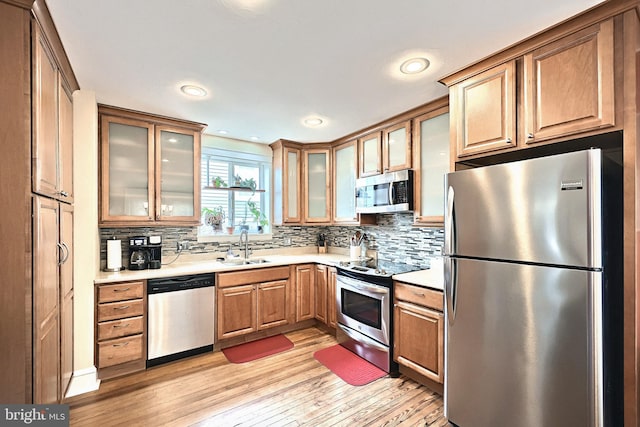 kitchen with tasteful backsplash, sink, light hardwood / wood-style flooring, and appliances with stainless steel finishes