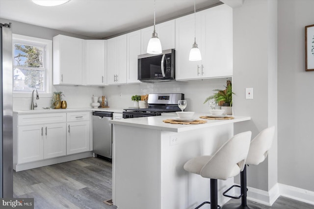 kitchen featuring hanging light fixtures, appliances with stainless steel finishes, white cabinets, and a kitchen bar