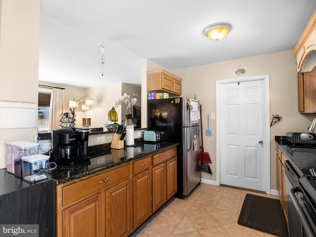 kitchen with dark stone counters, stainless steel fridge, and light tile patterned floors