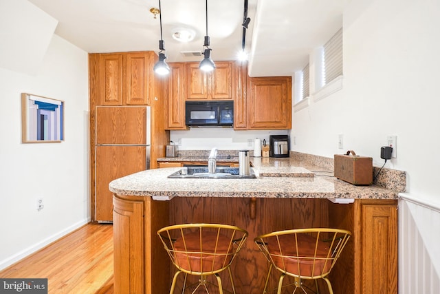 kitchen featuring pendant lighting, a breakfast bar area, paneled built in fridge, kitchen peninsula, and light wood-type flooring