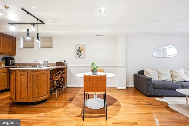 kitchen with sink, light hardwood / wood-style flooring, an island with sink, a kitchen bar, and decorative light fixtures