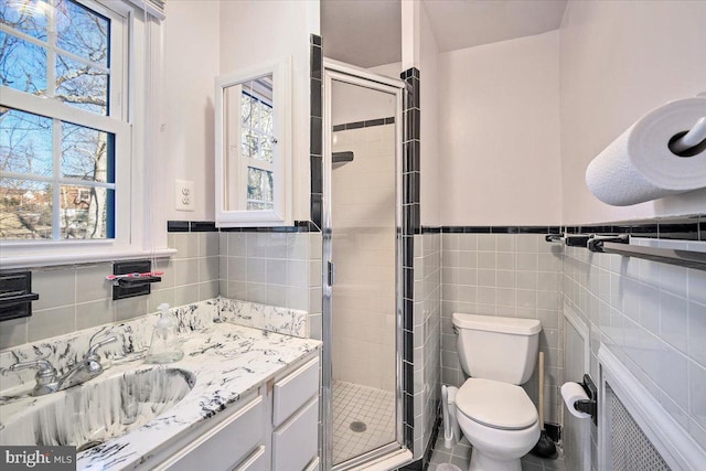 bathroom featuring vanity, toilet, a shower with shower door, and tile walls