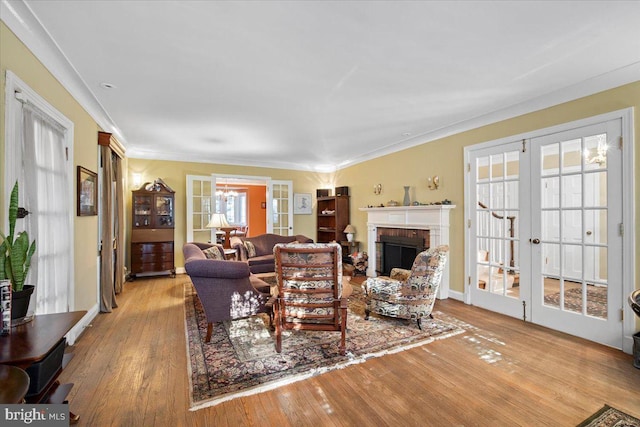 living room featuring crown molding, a brick fireplace, light hardwood / wood-style flooring, and french doors