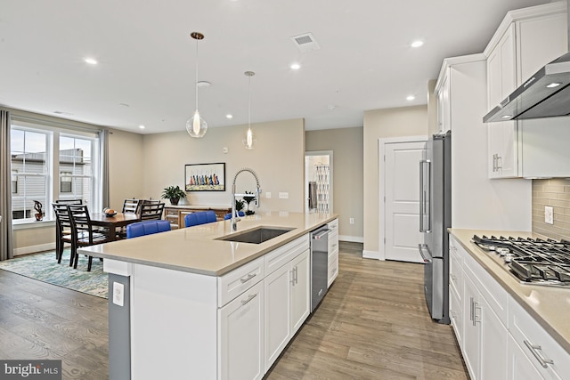 kitchen featuring sink, wall chimney range hood, hanging light fixtures, an island with sink, and white cabinets