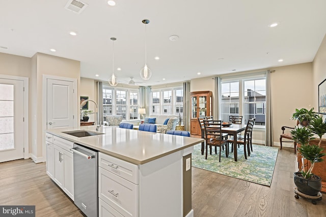 kitchen featuring pendant lighting, white cabinetry, dishwasher, sink, and a center island with sink