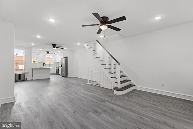 unfurnished living room featuring dark wood-style floors, recessed lighting, radiator, stairway, and baseboards