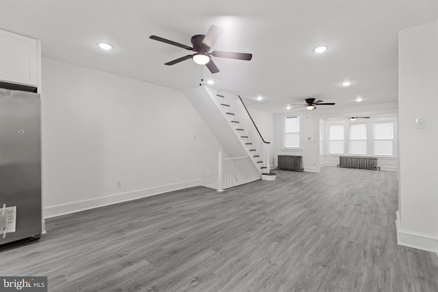 unfurnished living room featuring stairs, baseboards, radiator heating unit, and wood finished floors