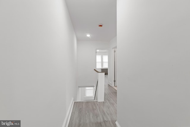 hall with light wood-style floors, radiator heating unit, baseboards, and an upstairs landing