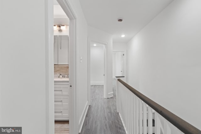 hallway with baseboards, wood finished floors, an upstairs landing, a sink, and recessed lighting