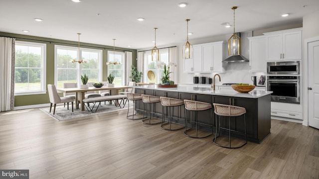 kitchen with a breakfast bar, decorative light fixtures, white cabinetry, stainless steel appliances, and a center island with sink