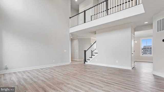 unfurnished living room featuring a high ceiling and light hardwood / wood-style flooring