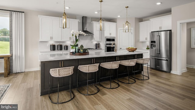 kitchen featuring white cabinetry, stainless steel appliances, a spacious island, decorative light fixtures, and wall chimney exhaust hood