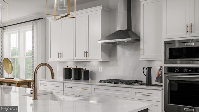 kitchen featuring sink, white cabinets, backsplash, stainless steel appliances, and wall chimney exhaust hood