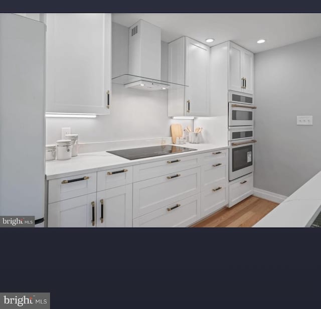 kitchen featuring wall chimney exhaust hood, white cabinetry, light wood-type flooring, double oven, and black electric stovetop