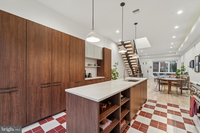 kitchen featuring pendant lighting, a skylight, sink, a kitchen island with sink, and light stone counters