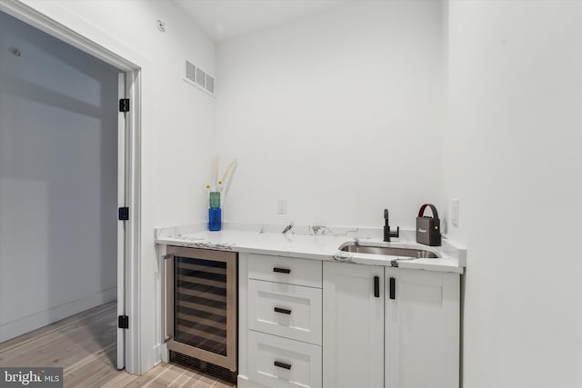 bar with sink, light hardwood / wood-style flooring, white cabinetry, wine cooler, and light stone countertops