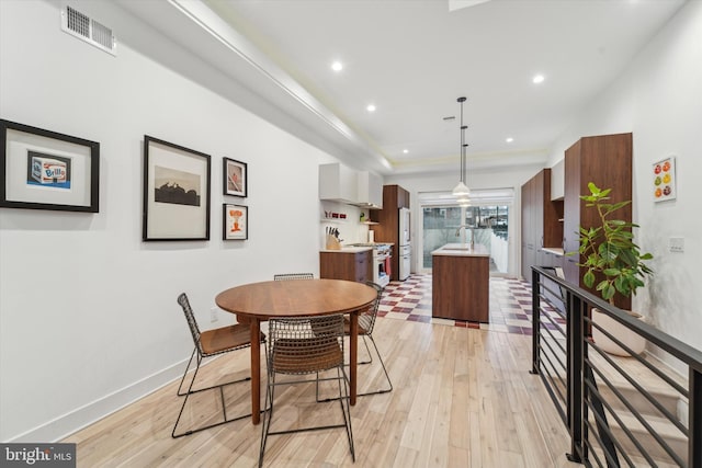 dining space with a tray ceiling, sink, and light hardwood / wood-style flooring