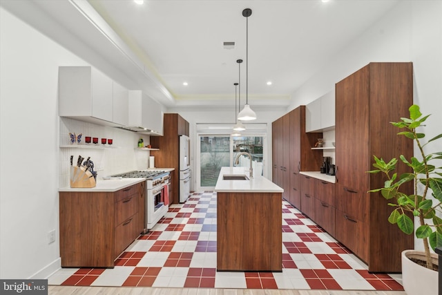 kitchen featuring sink, high end range, a kitchen island with sink, white cabinets, and decorative light fixtures