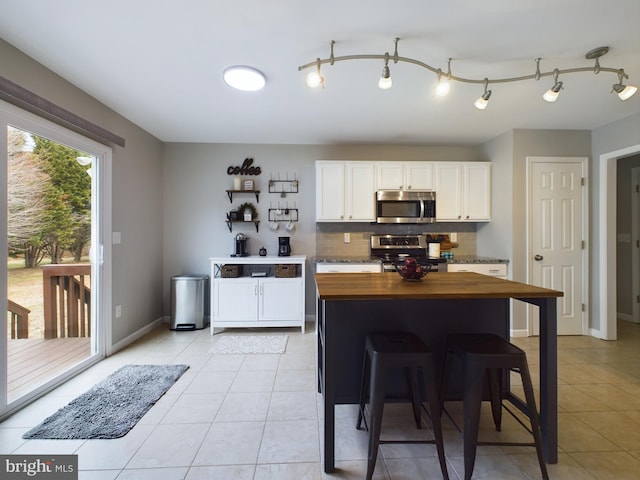 kitchen featuring wooden counters, light tile patterned floors, appliances with stainless steel finishes, white cabinets, and backsplash