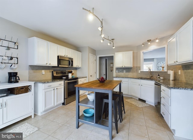 kitchen with stainless steel appliances, white cabinetry, dark stone countertops, and decorative backsplash