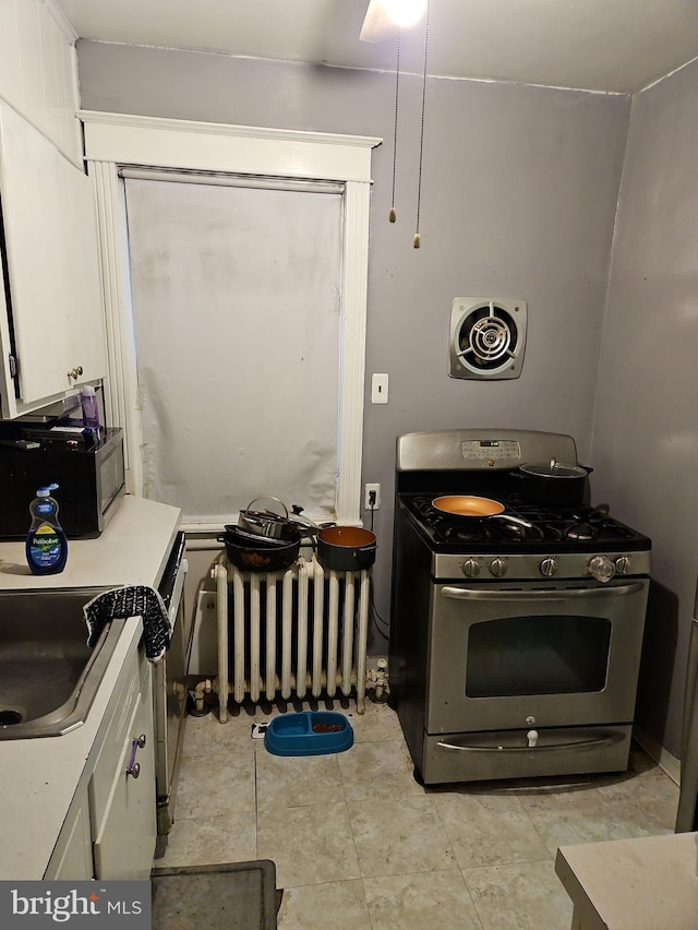 kitchen featuring stainless steel range with gas cooktop, sink, radiator heating unit, and white cabinets