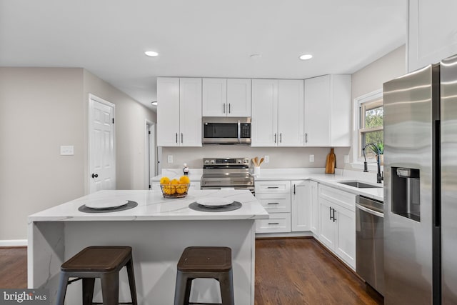 kitchen with a kitchen island, white cabinetry, sink, light stone counters, and stainless steel appliances