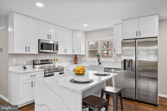 kitchen featuring sink, stainless steel appliances, a center island, white cabinets, and a kitchen bar