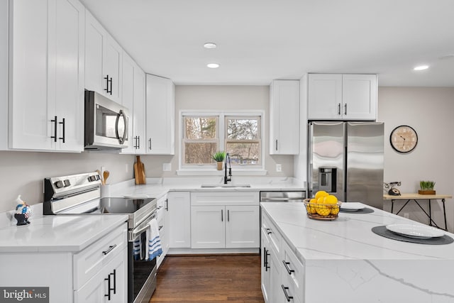 kitchen with sink, appliances with stainless steel finishes, dark hardwood / wood-style floors, light stone countertops, and white cabinets