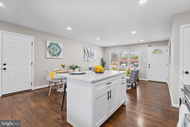 kitchen featuring dark wood-type flooring, a kitchen bar, a kitchen island, and white cabinets